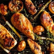 Grilled Tuscan Lemon Chicken features tender breasts and drumsticks on a grill pan, accompanied by charred lemon slices, mushrooms, and fresh thyme. The food boasts a glossy, caramelized appearance, showcasing meticulous seasoning and cooking.