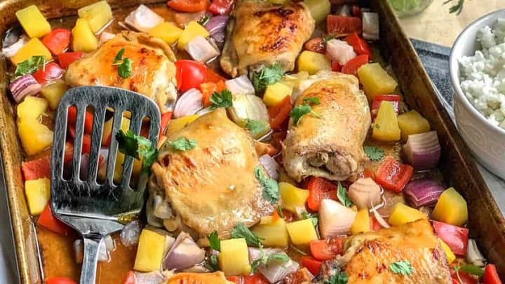 Sheet pan of chicken thighs with crispy skins with roasted onion, peppers and pineapple.