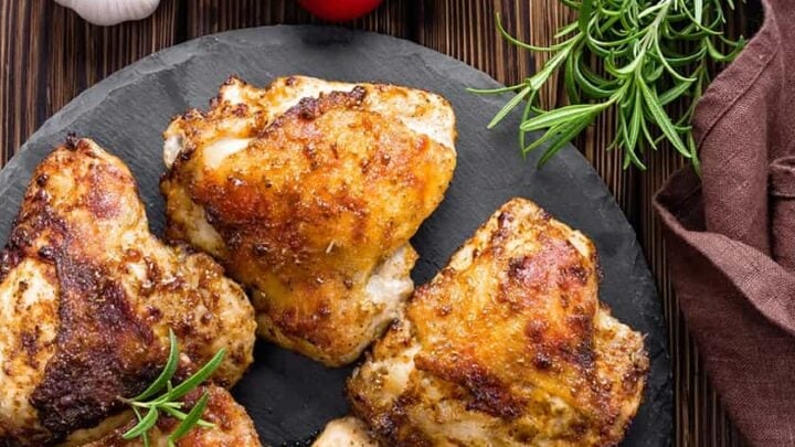 Top view of Grilled Lemon Chicken Thighs with Fresh Herbs on a black slate serving board with fresh tomatoes and rosemary sprigs.