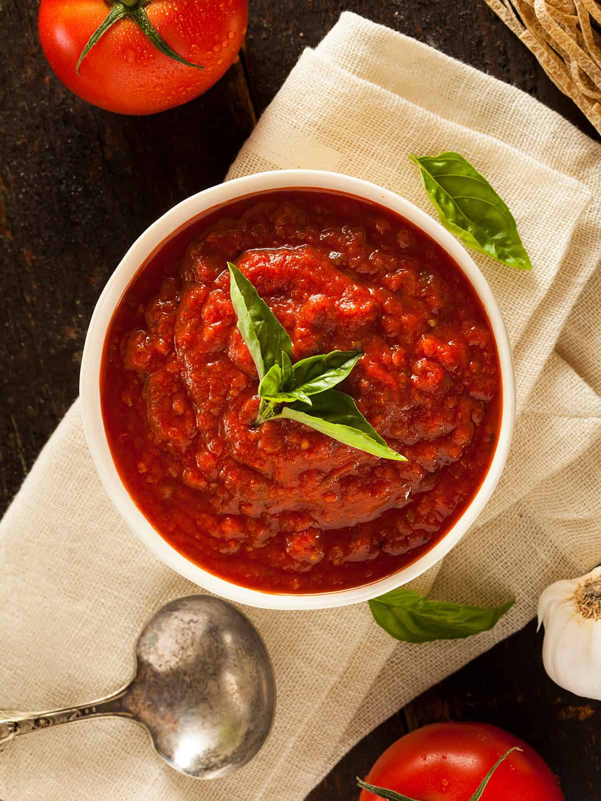 Bowl filled with Marcella Hazan's pasta sauce with sprigs of fresh basil and whole tomatoes nearby.