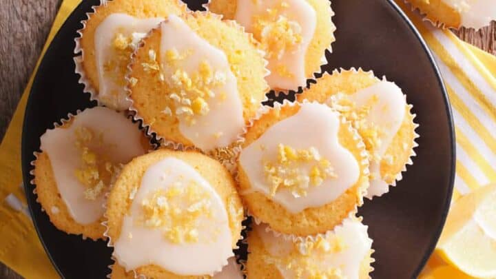 Greek Yogurt Lemon Muffins piled onto a black plate on a wooden background with yellow linens.