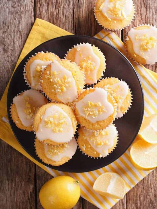 Greek Yogurt Lemon Muffins piled onto a black plate on a wooden background with yellow linens.