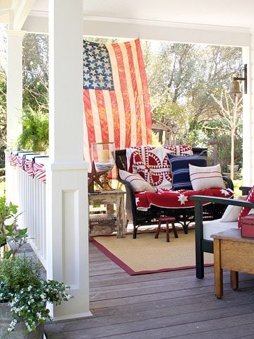 Patriotic porch setting with a U.S. flag, and seating with red, white and blue pillows and quilts.