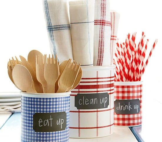 Three containers with checkered patterns set the mood for a 4th of July cookout. The blue one is filled with wooden cutlery labeled "eat up," the red holds striped straws for "drink up," and the white has napkins ready to help you "clean up.