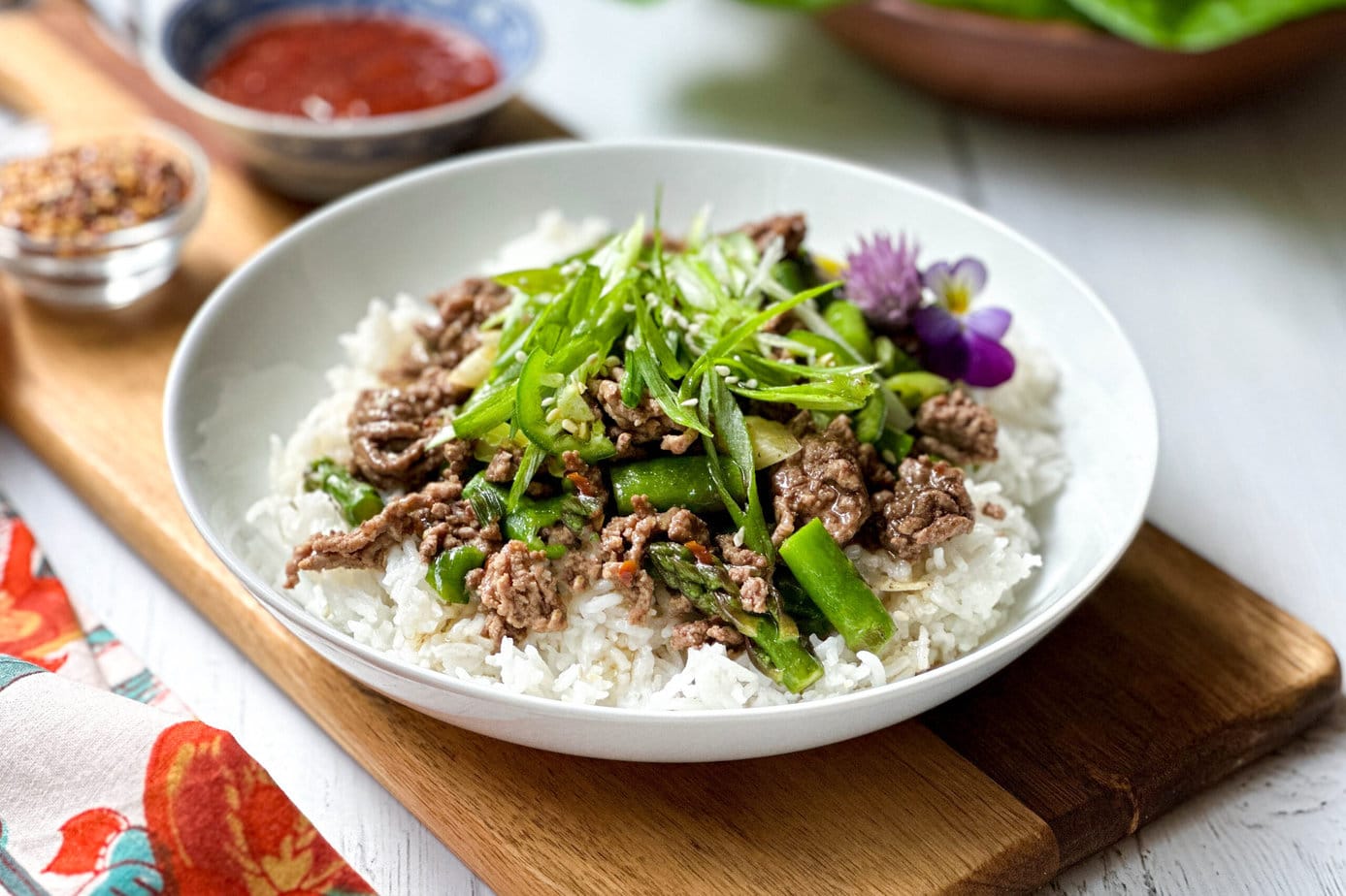 Closeup side view of Thai Ginger Ground Beef in a white bowl with asparagus and scallions
