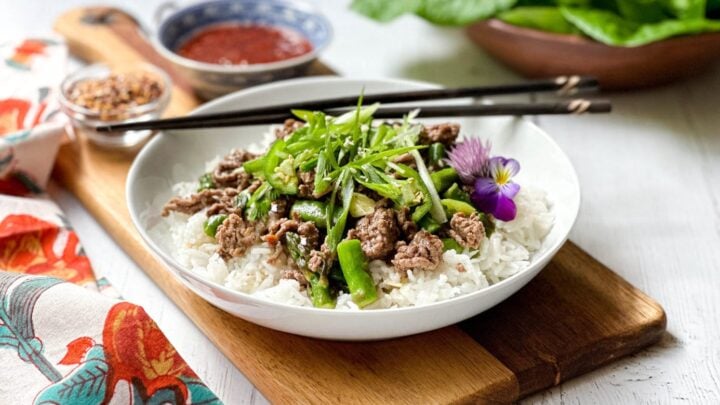 Side view of Thai Ginger Beef over basmati rice in a white bowl with chopsticks