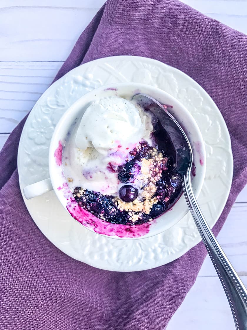 2 Minute Blueberry Crisp in a Mug close up served with a scoop of vanilla ice cream.