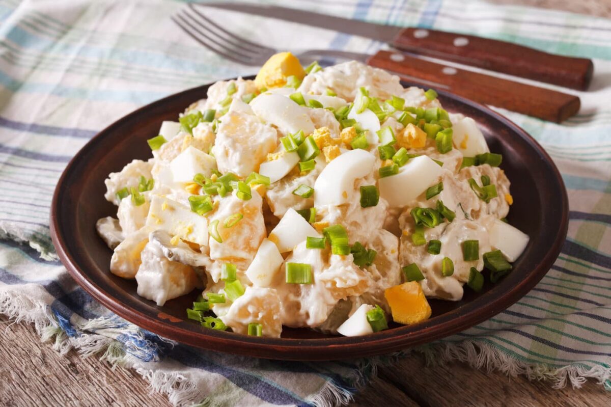 Side view of Classic Potato Salad in a dark wood bowl with green onions and boiled eggs