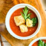 Bowl of slow cooker tomato soup topped with Parmesan croutons and parsley.