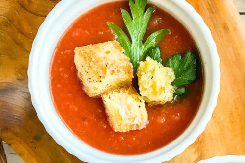 Bowl of slow cooker tomato soup topped with Parmesan croutons and parsley.
