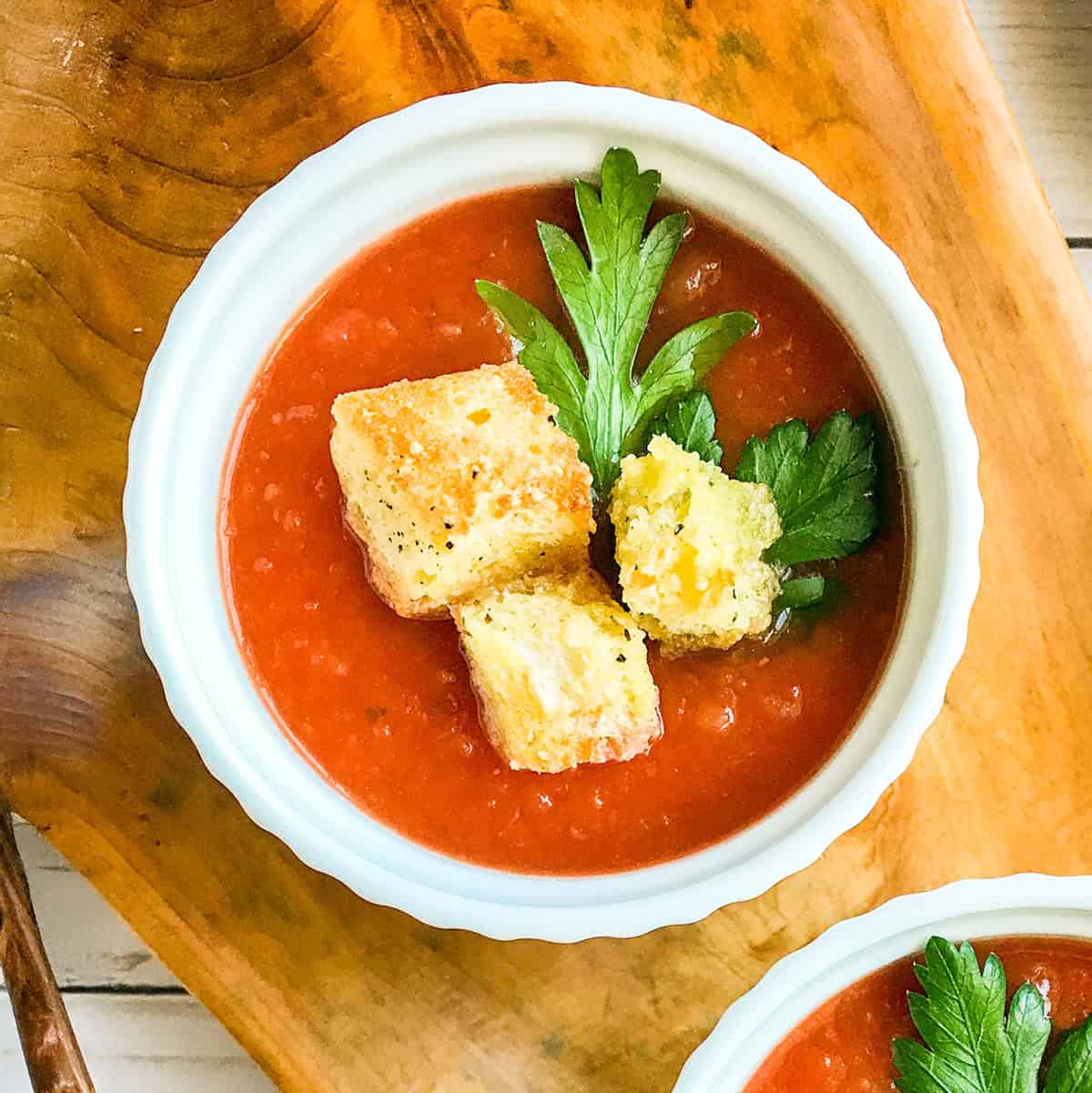Bowl of slow cooker tomato soup topped with Parmesan croutons and parsley.
