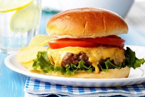 Side view of hamburger for Labor Day celebrations with melting cheese, lettuce and tomatoes slices on a white plate.