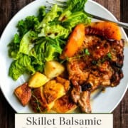A plate with skillet pork chops and peaches, roasted potatoes, fresh peach slices, and a green salad is beautifully displayed on a wooden table.