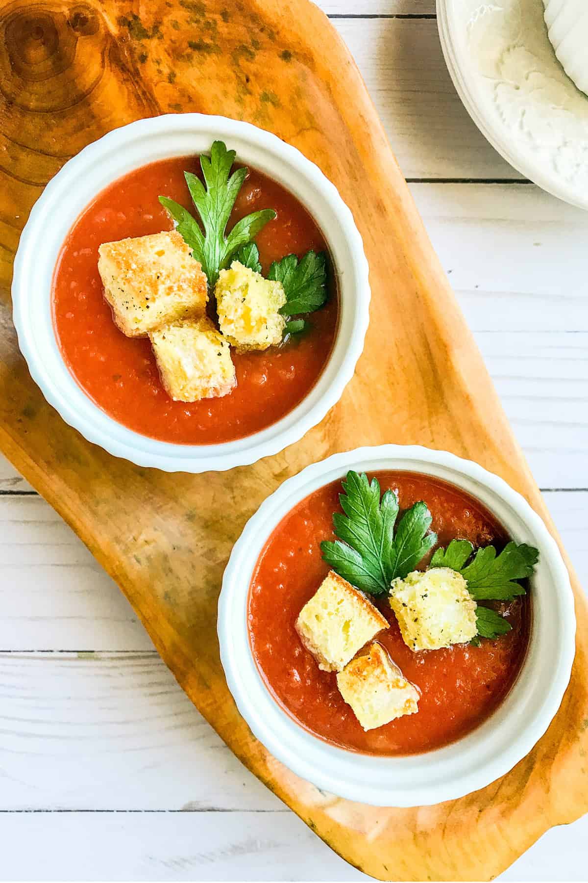Two bowls of slow cooker tomato soup with canned tomatoes topped with homemade croutons and parsley.