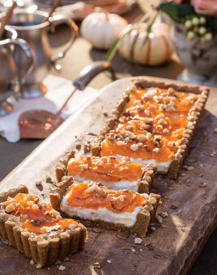 Rectangular tart with a crumb crust, creamy filling, and orange fruit topping, garnished with chopped nuts-perfect for an Autumn Afternoon Tea and beautifully displayed on a wooden board.