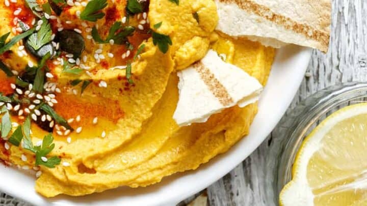 Closeup horizontal view of Roasted Pumpkin Hummus with fresh herbs and torn pieces of white pita.