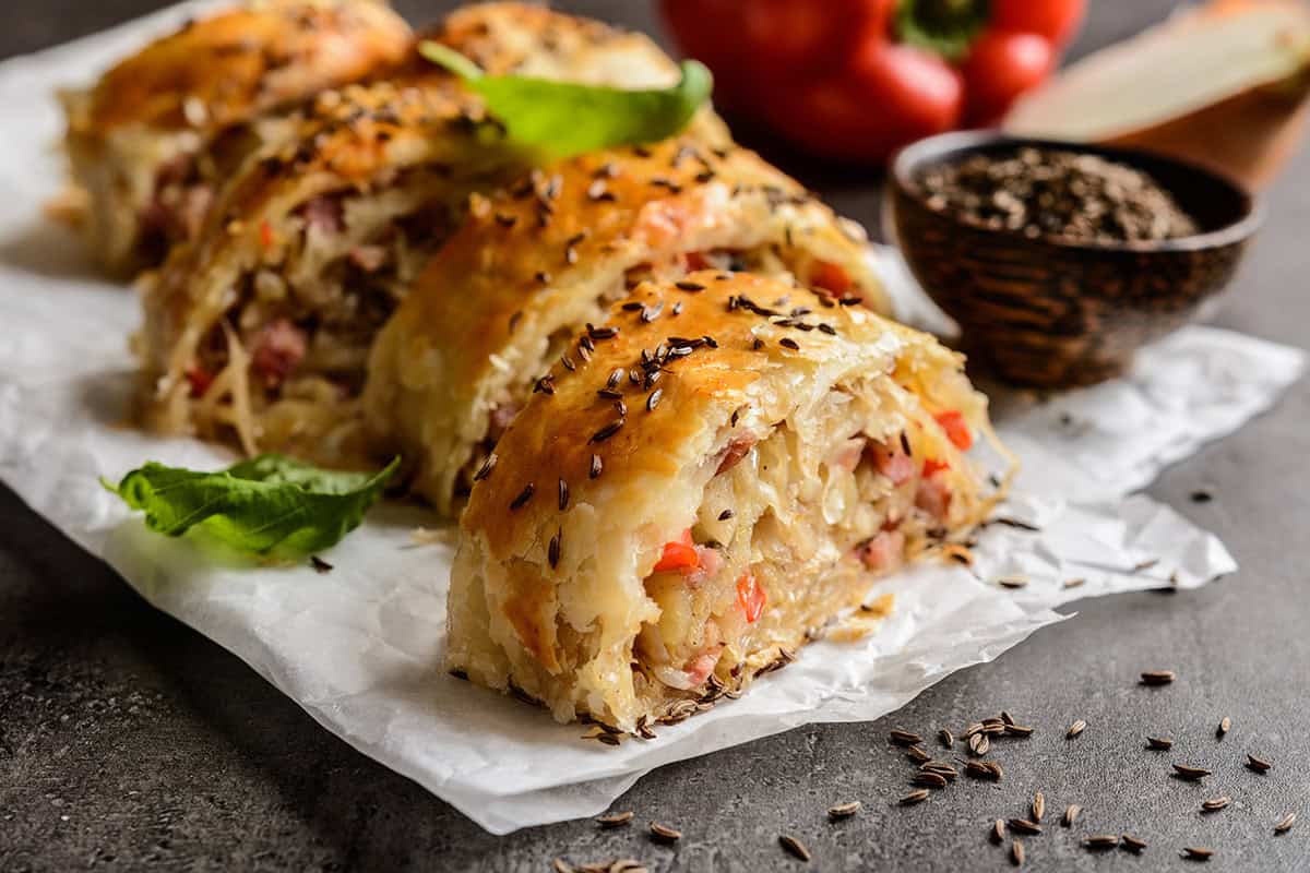 Closeup view of Krautstrudel slices on a parchment paper with caraway seeds.