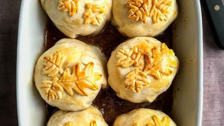 White baking dish of apple dumplings topped with pastry leaves.