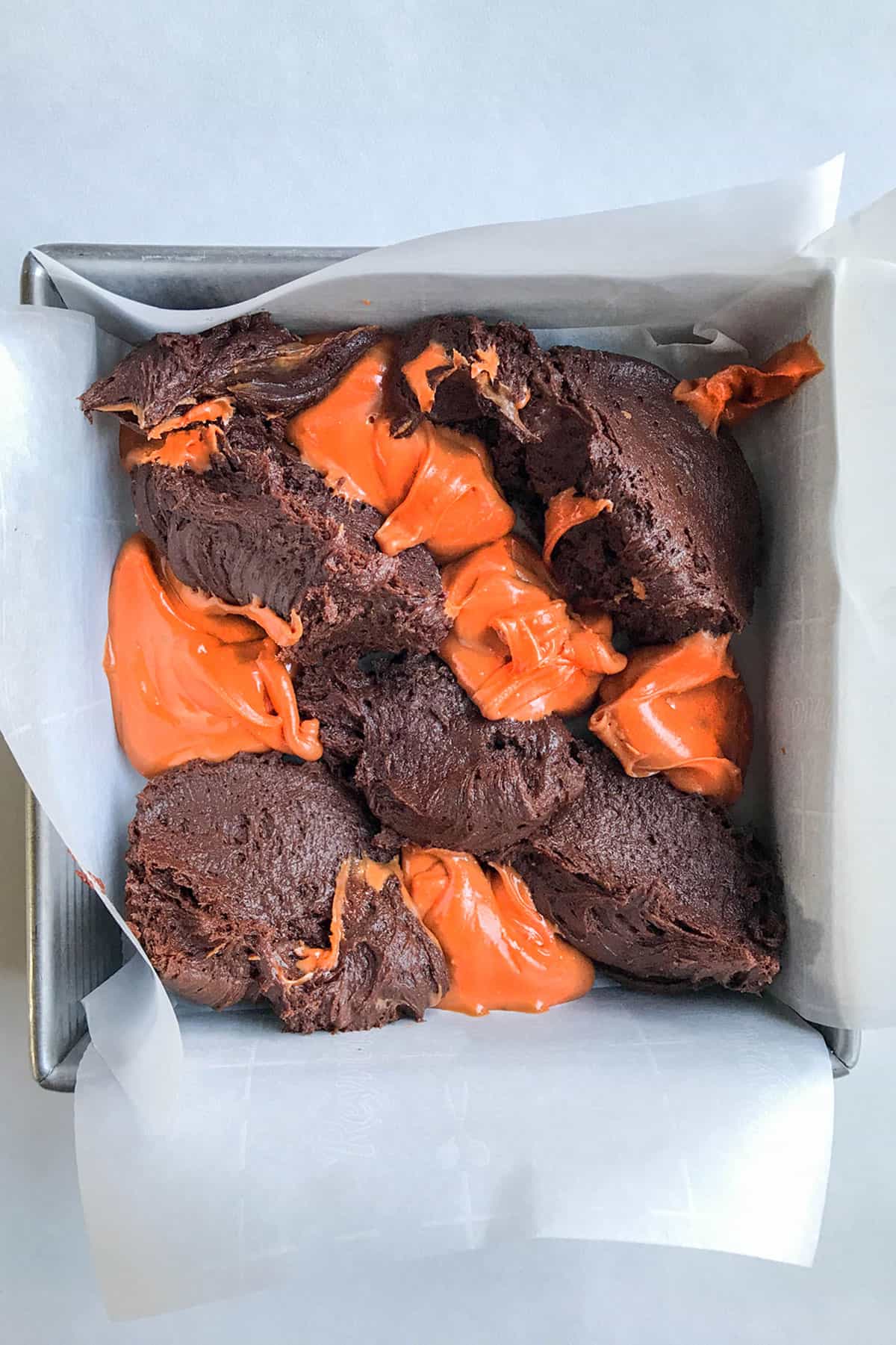 Top view of unbaked brownie batter with dollops of orange peanut butter and chocolate brownies ready for swirling.