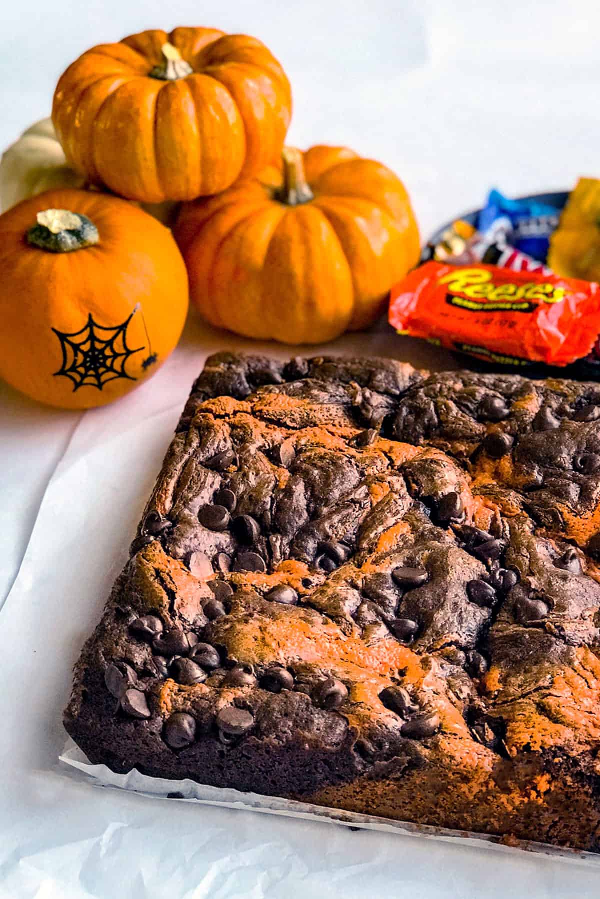Square of uncut, baked peanut butter chocolate swirl brownies with Halloween pumpkins and candy in the background.
