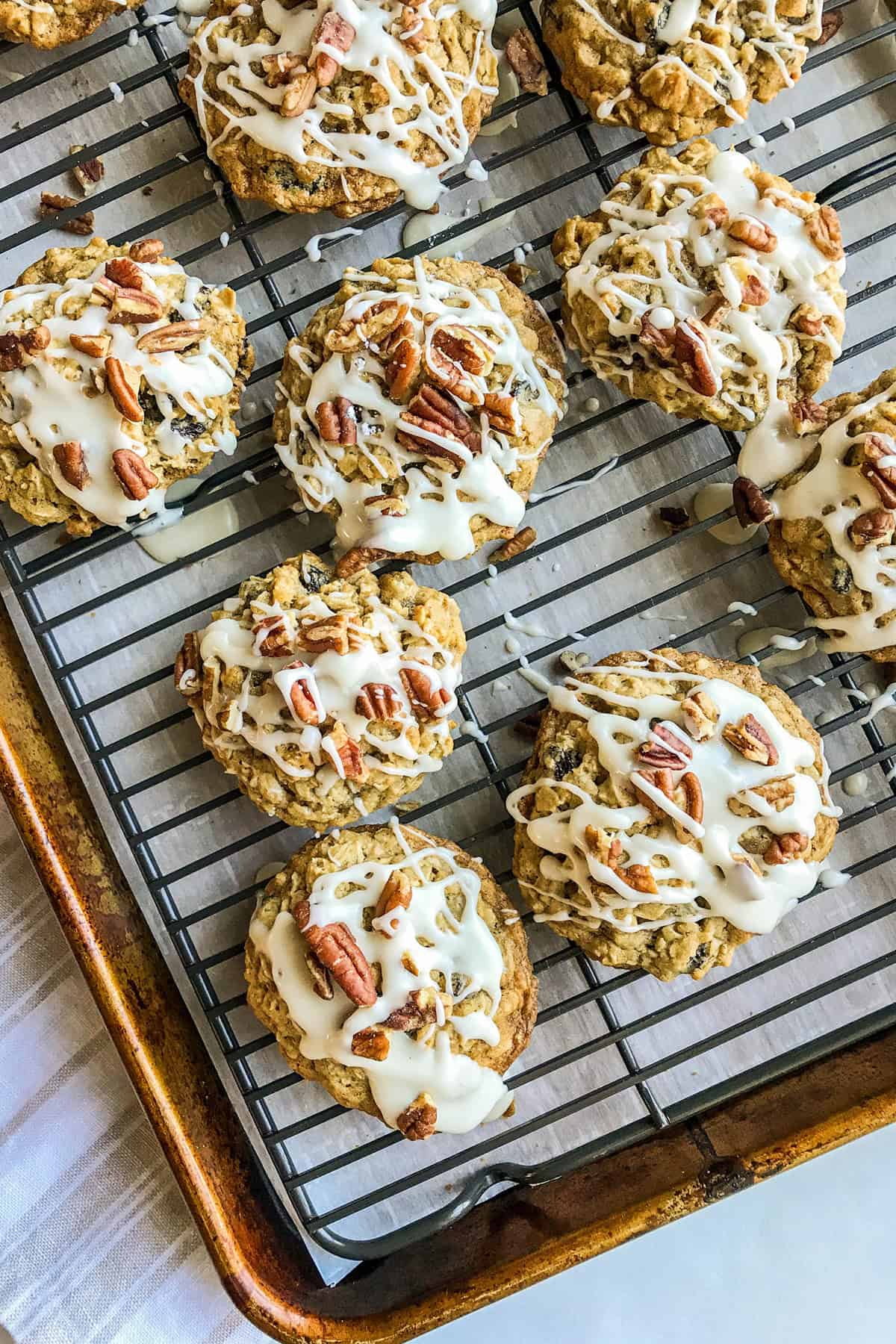 Oatmeal Raisin cookies on a rack lined cookie sheet being drizzled with maple glaze.