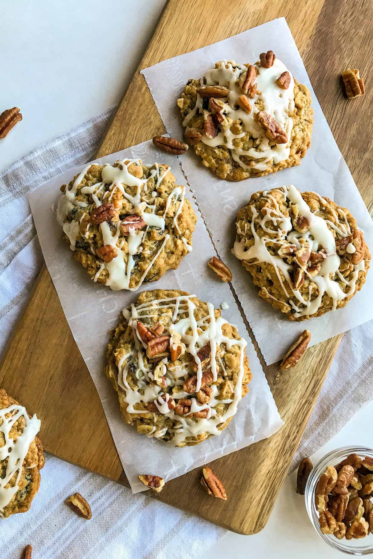 Glazed oatmeal raising cookies with toasted pecans on a parchment lined wooden board.