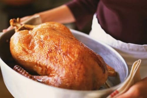 Person holding a roasted whole turkey in a metal roasting pan, using a dish towel for grip-a classic example of German Christmas food.