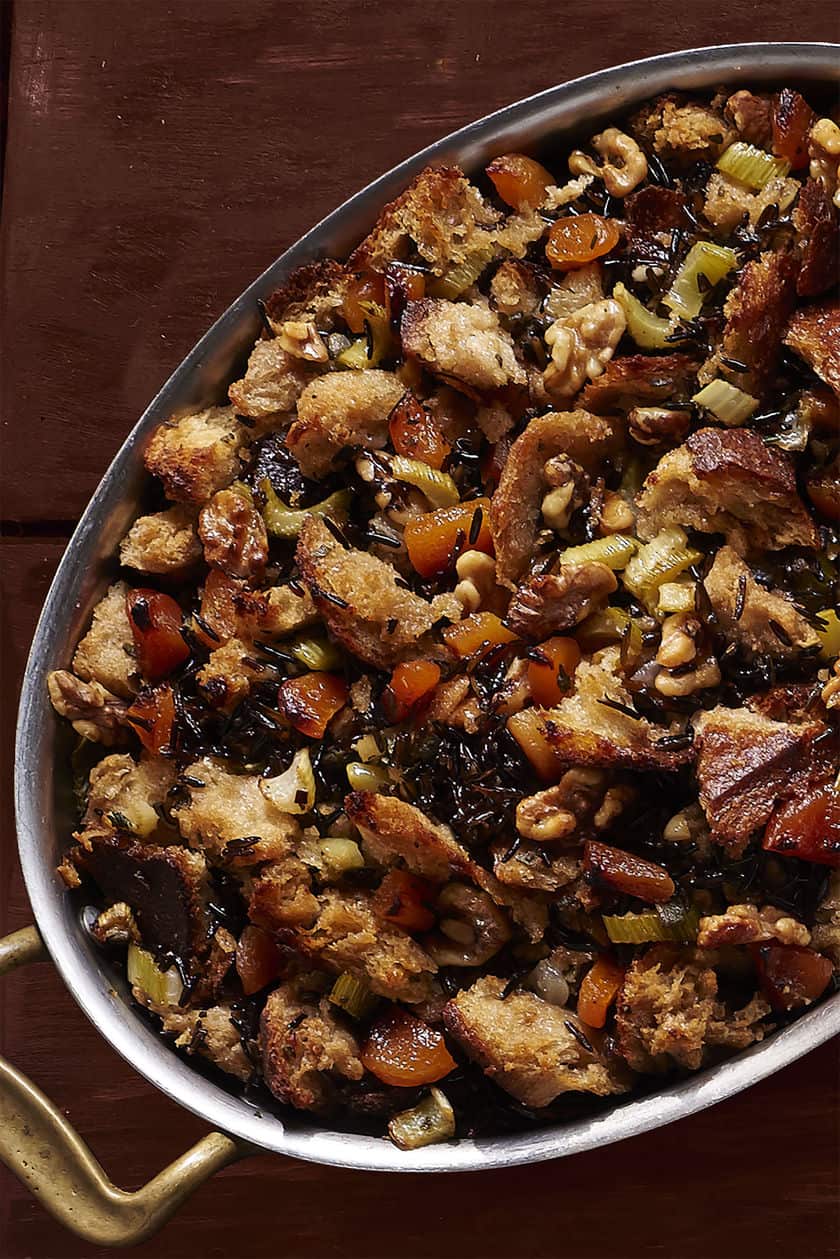 Oval baking dish filled with bread stuffing, a delicious mix of carrots, celery, wild rice, and walnuts-perfect inspiration for your thanksgiving stuffing recipes-set on a dark wooden surface.