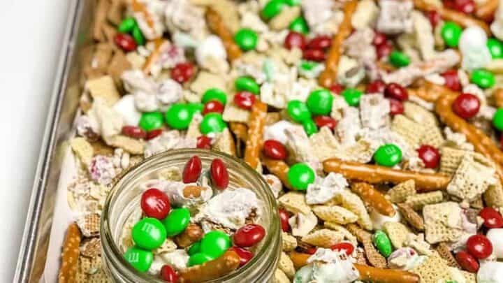 Tray of chex mix with pretzel sticks with a glass jar also full of mix.