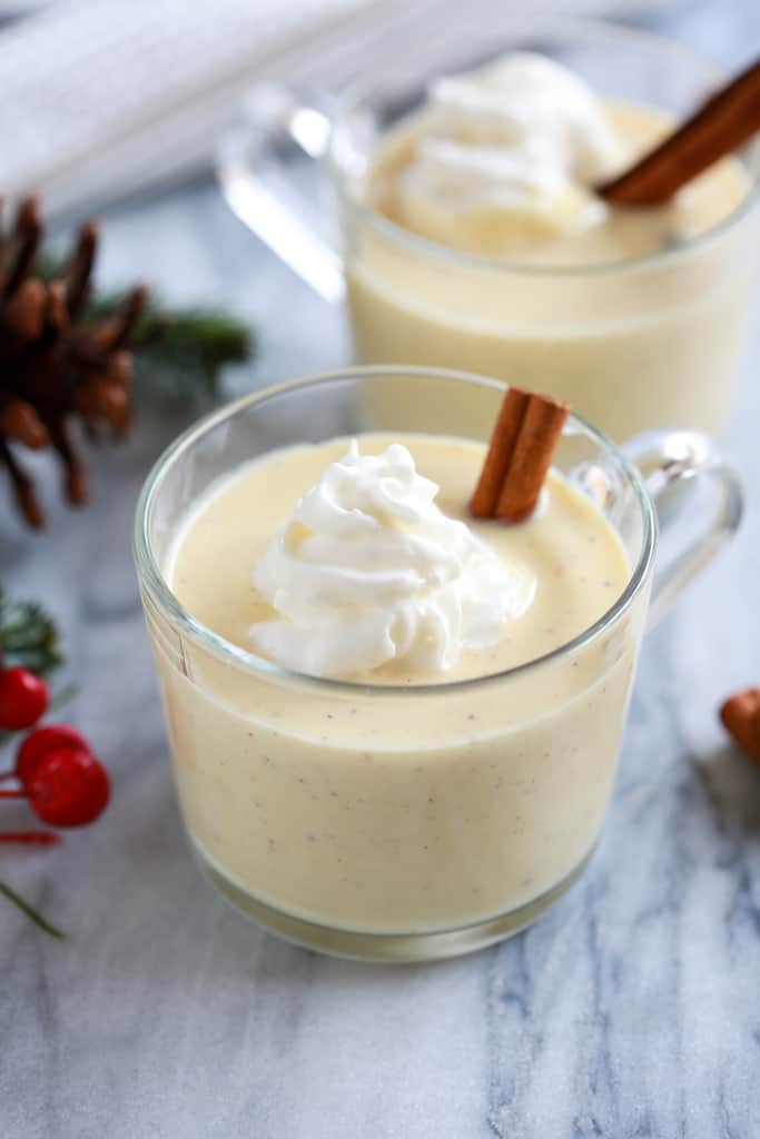Glass of homemade eggnog with a cinnamon stick and whipped cream.
