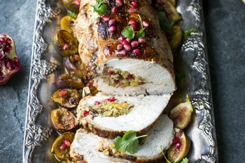 Sliced stuffed roast turkey, perfect for Christmas dinner, is garnished with pomegranate seeds and herbs, served on a silver tray with figs and pomegranate halves.