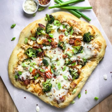 Square image of homemade Teriyaki Chicken Pizza with fresh chopped green onions, Parmesan cheese, and red pepper flakes for serving.