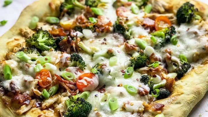 Pizza topped with teriyaki sauce, chicken, broccoli, bacon, cherry tomatoes and cheese.