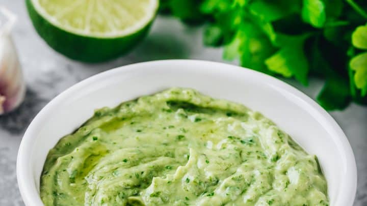 5 Minute Avocado Hummus Recipe in a white bowl with halved limes and fresh cilantro.