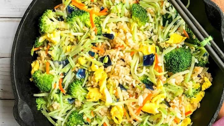 Top view of Fried Rice with Broccoli Cabbage Slaw in a black skillet with brown chop sticks on a wooden cutting board.