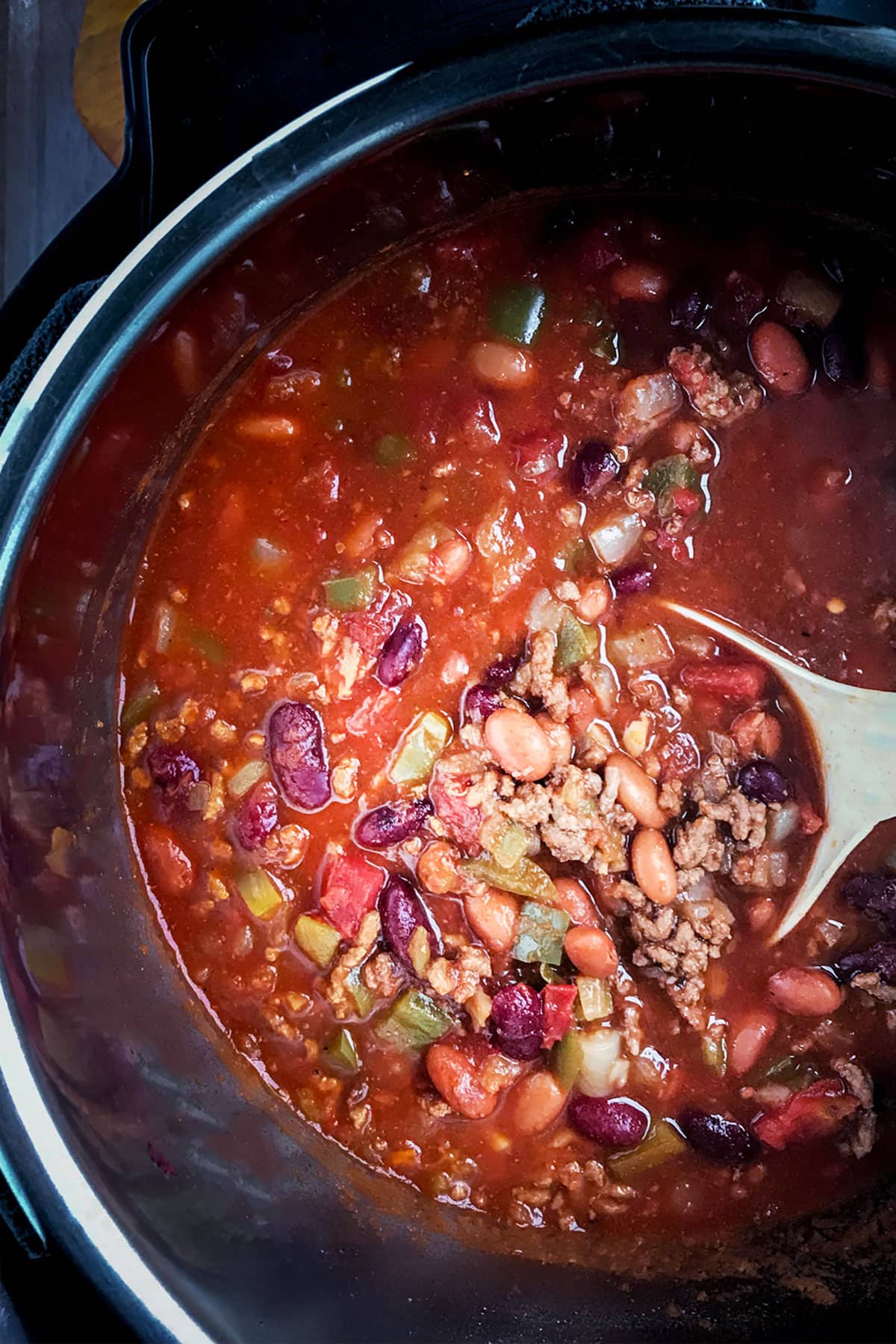 Instant Pot Chili in the pressure cooker insert with a white spoon mashing the beans for extra thickness.