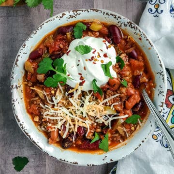 Bowl of Instant Pot chili topped with sour cream, shredded cheese and fresh cilantro.