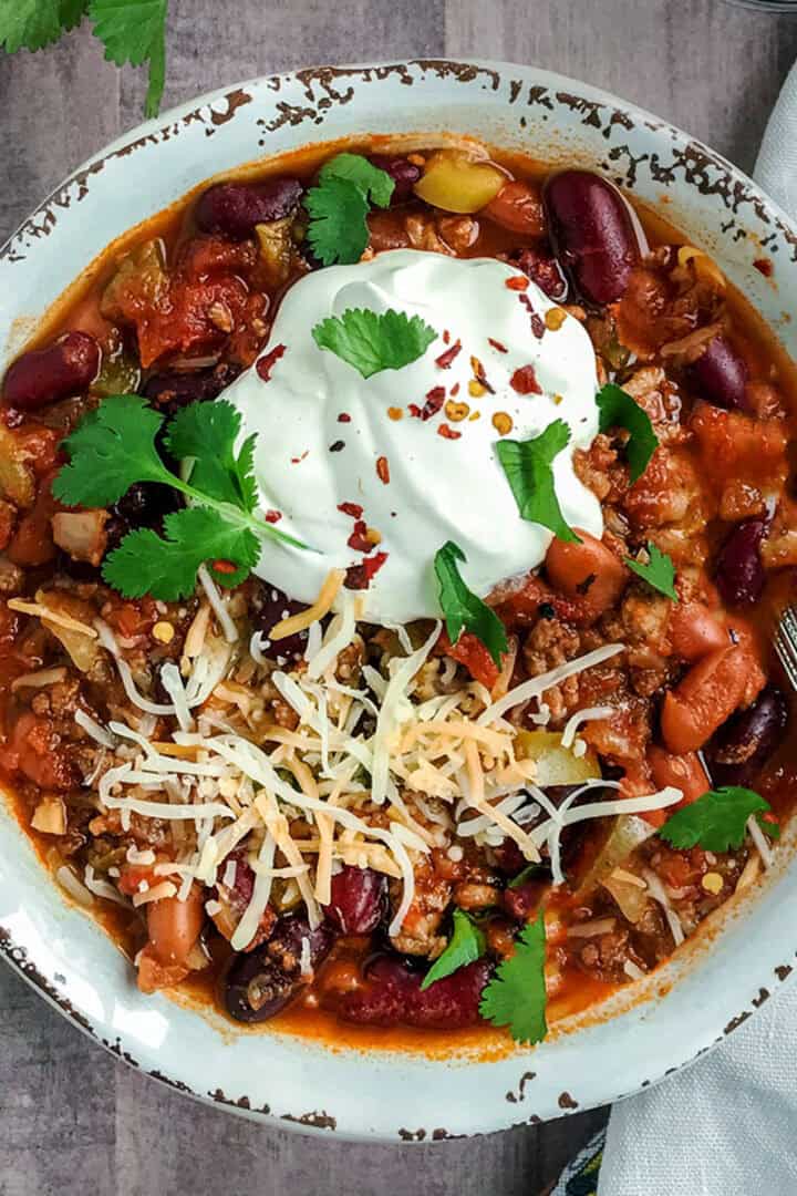 Bowl of Instant Pot chili topped with sour cream, shredded cheese and fresh cilantro.