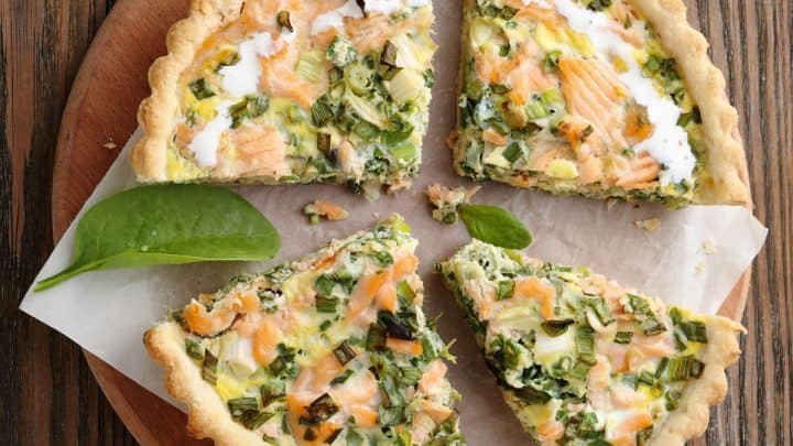 Salmon Quiche cut into slices on a wooden serving board.