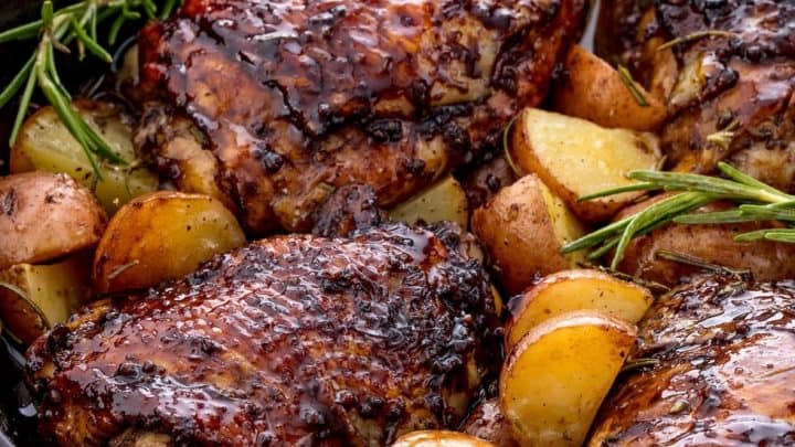 A cast iron skillet filled with glazed roasted chicken thighs, potato wedges, and sprigs of rosemary—an irresistible choice for Father's Day Recipes.