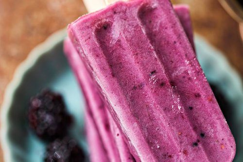 closeup of 2 blackberry popsicles on a blue plate
