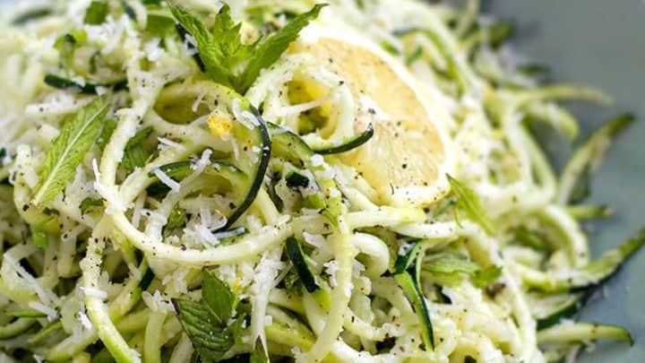 A bowl of zucchini noodles topped with grated cheese, lemon slice, and fresh herbs, served on a light blue plate—perfect for refreshing summer Instant Pot recipes.