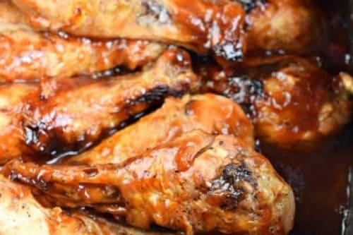 Several cooked chicken drumsticks coated in a glossy barbecue sauce are arranged closely together in a baking dish, making this the perfect Summer Slow Cooker meal for easy gatherings.