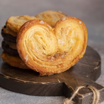 Square image of Palmier on dark wooden serving board with more stacked behind.