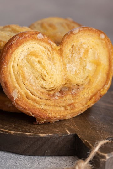 Square image of Palmier on dark wooden serving board with more stacked behind.