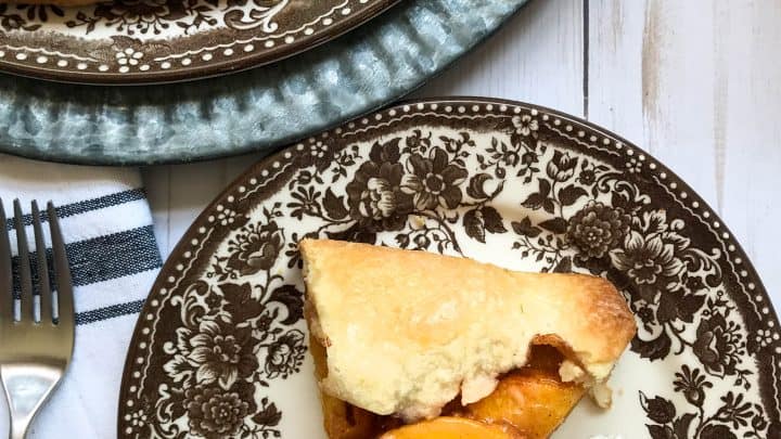 Side closeup view of warm apple crisp serving in a white bowl with melting vanilla ice cream