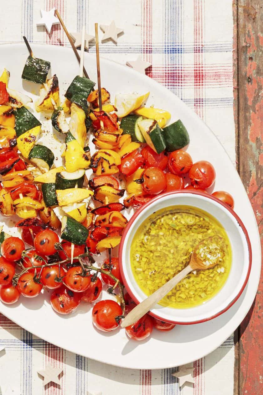 Grilled vegetable skewers with zucchini, bell peppers, and cherry tomatoes served on a white platter with a bowl of yellow dipping sauce and a wooden spoon-perfect for your next Game Day Recipes lineup.