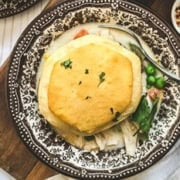 A plate of slow cooker chicken pot pie topped with a biscuit, served with mixed vegetables and a spoon on a decorative plate.