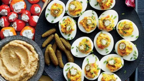 A platter of Game Day Appetizers featuring deviled eggs, cheese, breadsticks, carrot sticks, cherry peppers with cheese, pickles, prosciutto-wrapped bites, hummus, and radicchio leaves—arranged neatly for the perfect party spread.