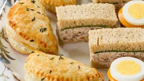 A plate with assorted tea sandwiches, halved savory pastries, and round slices of hard-boiled egg with cheese on a decorative platter—perfect for a classic Scottish Afternoon Tea.